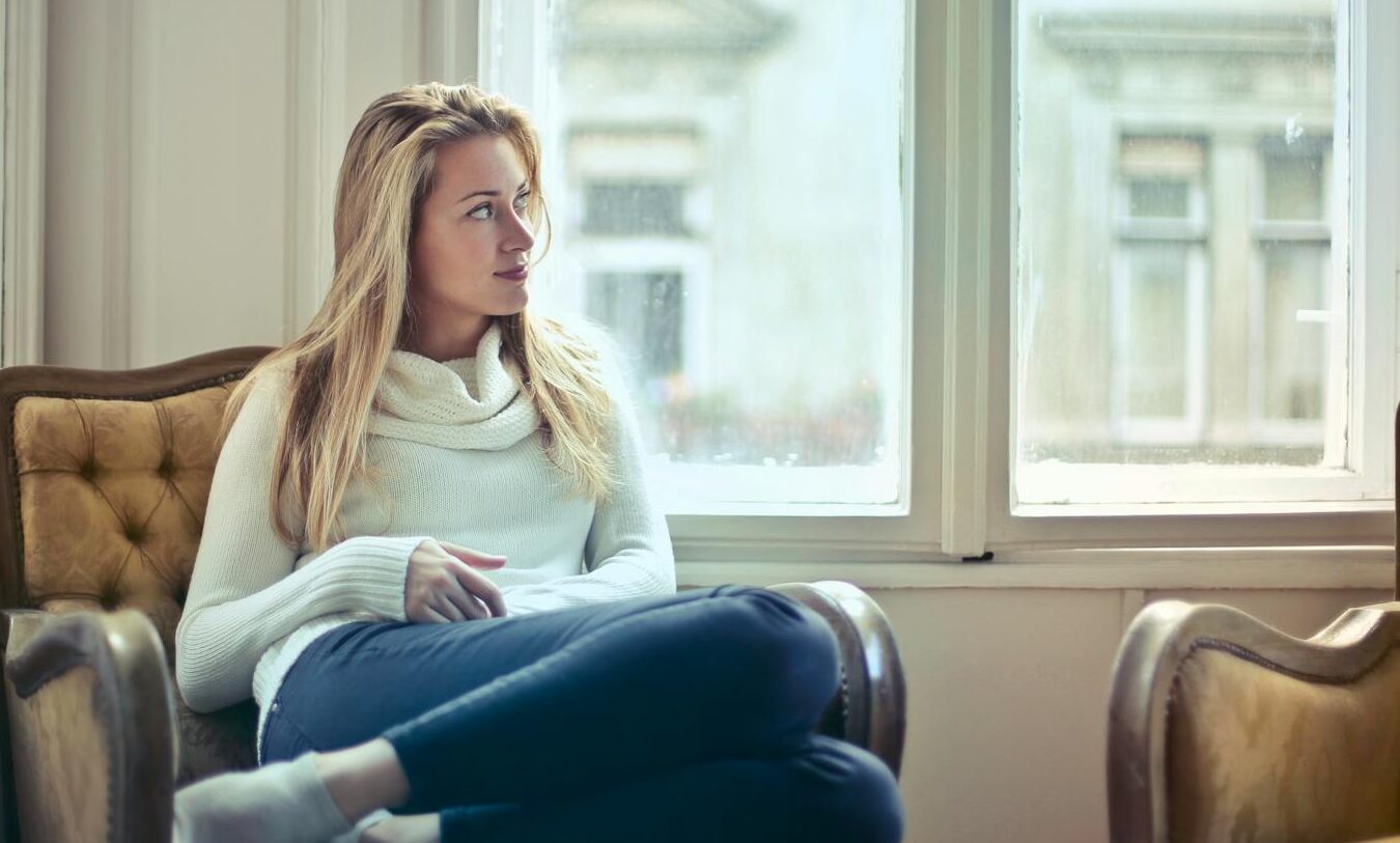 A serene moment of a woman in a cosy room, enjoying leisure time by the window.